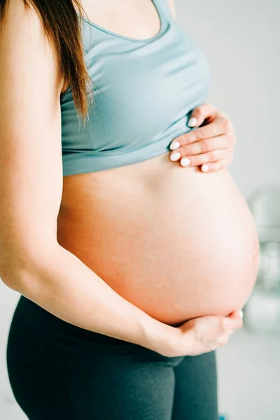 Terhes lány sportruházatban öleli a csupasz hasát a stúdióban — Stock Fotó