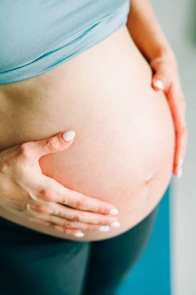 Terhes lány sportruházatban öleli a csupasz hasát a stúdióban — Stock Fotó