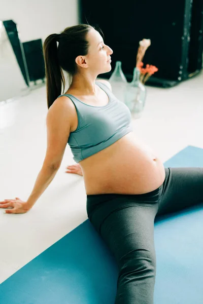 Una joven hermosa embarazada en ropa deportiva está haciendo yoga, realizando ejercicios sentados en una alfombra en el estudio — Foto de Stock