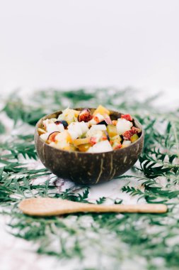 Masanın üzerinde tropikal yapraklarla hindistan cevizi kabuğu kabuğu içinde sağlıklı meyve salatası. vejetaryen yemeği