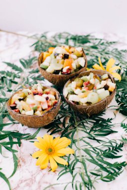 Masanın üzerinde tropikal yapraklarla hindistan cevizi kabuğu kabuğu içinde sağlıklı meyve salatası. vejetaryen yemeği