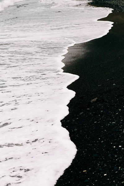 Uma onda do mar chega na costa com areia vulcânica preta. belo fundo natural na Islândia — Fotografia de Stock