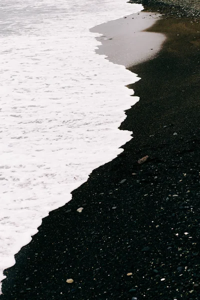 Uma onda do mar chega na costa com areia vulcânica preta. belo fundo natural na Islândia — Fotografia de Stock