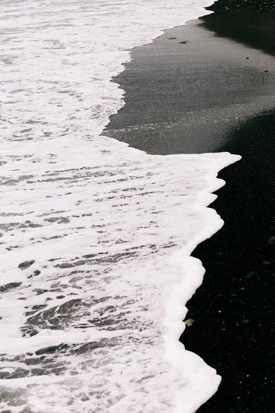 Una ola de mar llega a la orilla con arena volcánica negra. hermoso fondo natural en Islandia —  Fotos de Stock