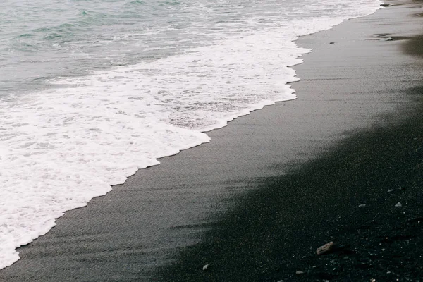 Een zeegolf komt aan op de kust met zwart vulkanisch zand. mooie natuurlijke achtergrond in IJsland — Stockfoto