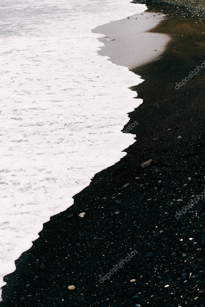 a sea wave arrives on the shore with black volcanic sand . beautiful natural background in Iceland