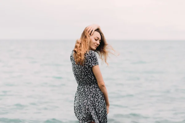 A young girl in a dress from the back stands on the beach on large stones — Stok fotoğraf