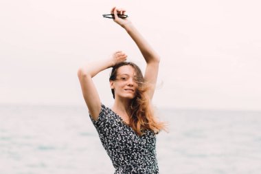 a young girl in a dress stands on the beach on large stones, the wind develops her hair