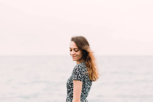 Молода дівчина в сукні ззаду стоїть на пляжі на великих каменях — стокове фото