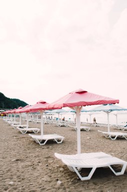 white sunbeds with colorful umbrellas on a pebble beach in the summer
