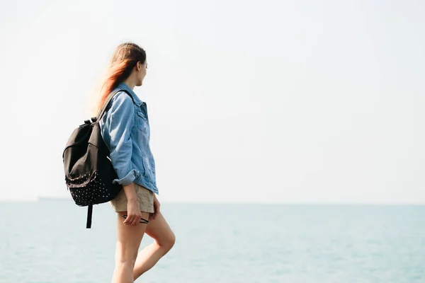 Молода дівчина мандрівник з рюкзаком ходить босоніж на великих каменях на узбережжі моря — стокове фото