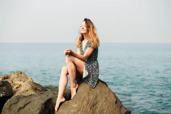 Молода красива дівчина в сукні на великих каменях, мальовниче місце на узбережжі моря — стокове фото