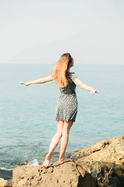 Молода красива дівчина в сукні на великих каменях, мальовниче місце на узбережжі моря — стокове фото