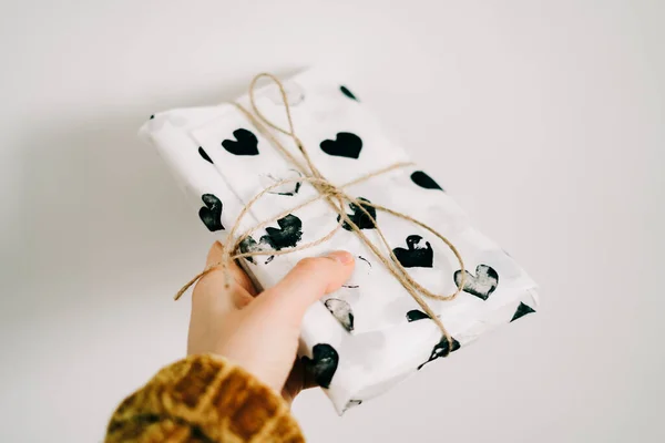 A gift in a woman's hand wrapped in homemade wrapping paper with black hearts for Valentine's day — Stockfoto