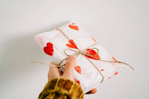 A gift in a woman's hand wrapped in homemade wrapping paper with red hearts tied with jute thread for Valentine's day — Stockfoto