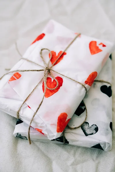 Deux cadeaux enveloppés dans du papier d'emballage fait maison avec des coeurs rouges et noirs attachés avec du fil de jute pour la Saint-Valentin sur une table blanche — Photo