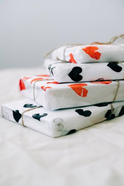 Sevgililer günü için beyaz bir masada kırmızı ve siyah kalplerle sarılı ev yapımı ambalaj kağıdına sarılı bir yığın hediye.