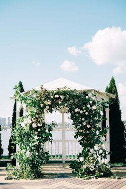 Düğün kemeri, güzel bir çiçek düzeniyle süslenmiş. Güneşli bir günde, taze yeşillik dalları.