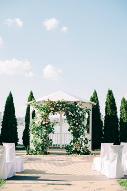 Düğün kemeri, güzel bir çiçek düzeniyle süslenmiş. Güneşli bir günde, taze yeşillik dalları.
