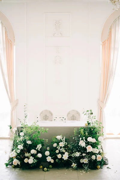 Virágos elrendezése fehér finom virágok és friss növényzet a tervezés az esküvői asztal a menyasszony és a vőlegény a fehér teremben — Stock Fotó