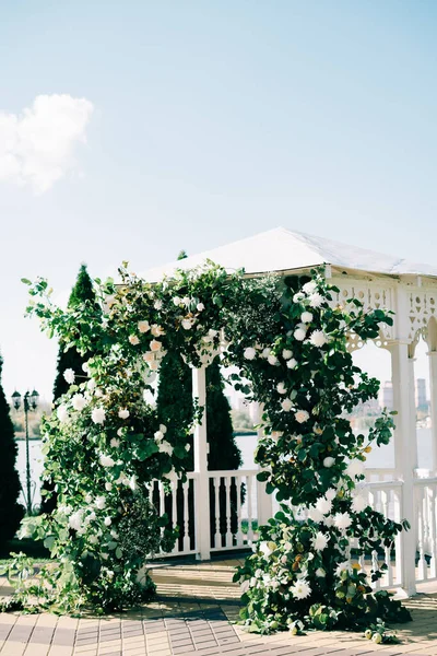 Wedding arch decorated with a beautiful floral arrangement of white flowers and fresh branches of greenery on a Sunny day — Stock Photo, Image