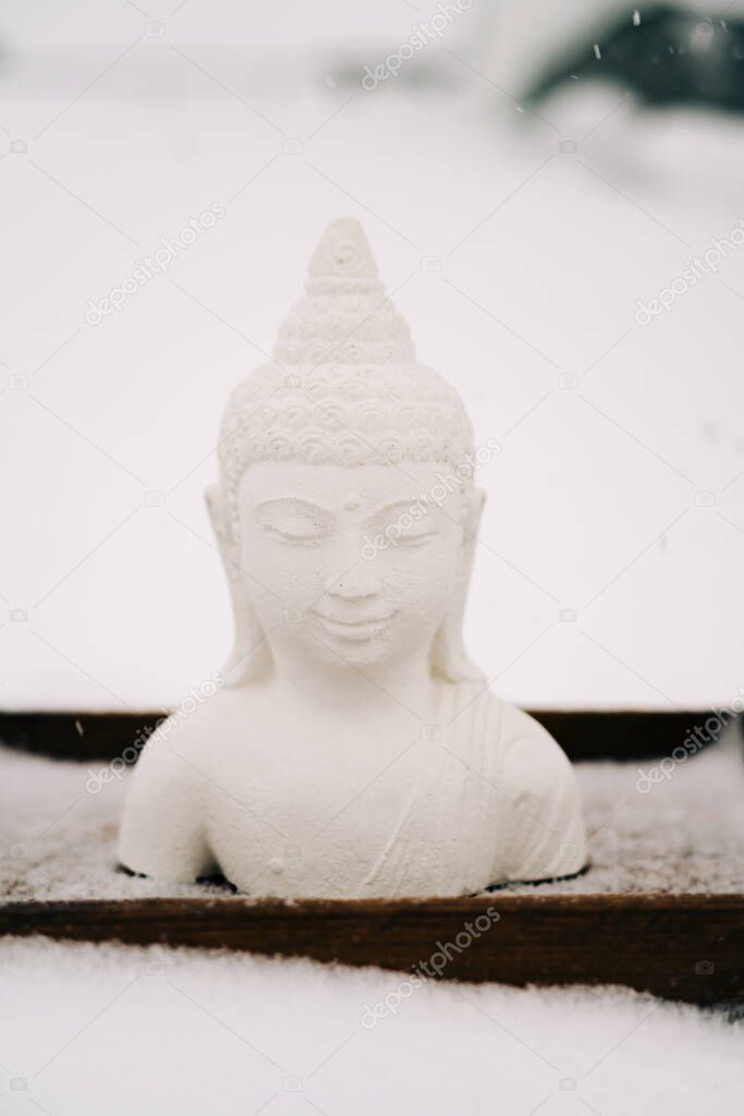 white Buddha figurine made of plaster on a wooden stand during a snowfall