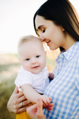 Genç ve mutlu bir anne, kollarında küçük bir çocuk, nazikçe kafasına yaslanıyor, bir samanlığın ortasında duruyor gün batımının ışınlarında toplanmış samanlığın yanında.