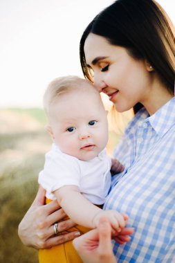 Kollarında küçük bir çocukla genç mutlu bir anne, nazikçe başını öpüyor, batan güneşin ışınlarıyla bir tarlanın ortasında duruyor.