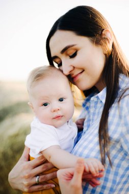 Genç ve mutlu bir anne, kollarında küçük bir çocuk, nazikçe kafasına yaslanıyor, bir samanlığın ortasında duruyor gün batımının ışınlarında toplanmış samanlığın yanında.