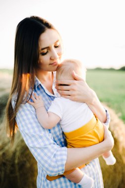 Kollarında küçük bir çocukla genç ve güzel bir anne, altın gün batımının ışınlarında toplanmış samanlığın yanındaki bir tarlanın ortasında elbise içinde dikiliyor.