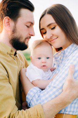 Mutlu genç bir ailenin portresi, anne ve babanın birbirine sarıldıkları, gün batımında küçük çocuklarını aralarında tuttukları,