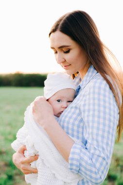 Mavi elbiseli genç bir annenin portresi, batan güneşin ışınlarında, küçük bir çocuğu göğsüne bastırıyor.