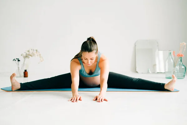 Spor kıyafetleri içinde genç ve güzel bir kız yoga yapıyor, halının üzerinde egzersiz yapıyor.