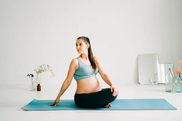 Spor kıyafetleri içinde genç ve güzel bir kız yoga yapıyor, halının üzerinde egzersiz yapıyor.