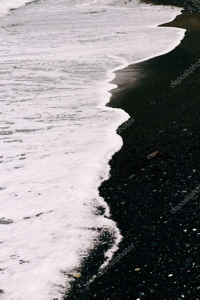 a sea wave arrives on the shore with black volcanic sand .