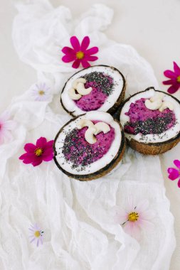 Pembe çiçekli Hindistan cevizi tabağında fındık ve Chia tohumlu sağlıklı kahvaltı meyveli smoothie.