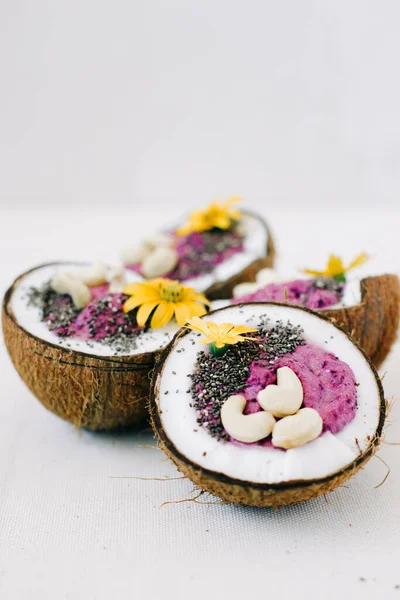 Sarı çiçeklerle süslenmiş hindistan cevizi tabağında fındık ve Chia tohumlu sağlıklı kahvaltı meyveli smoothie.