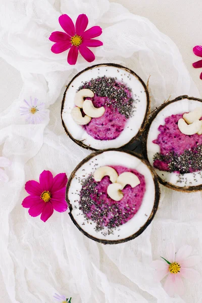 Pembe çiçekli Hindistan cevizi tabağında fındık ve Chia tohumlu sağlıklı kahvaltı meyveli smoothie.