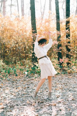 Güz ormanı arasında, beyaz elbiseli ve şapkalı güzel bir genç kız.