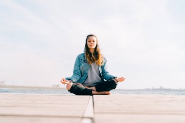 Genç ve güzel bir kız gölün yanındaki iskelede oturuyor ve meditasyon yapıyor.