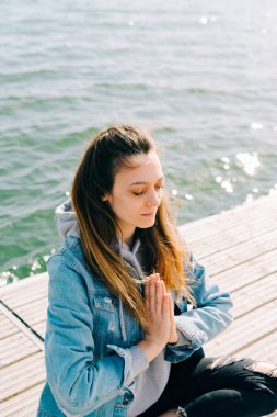 Genç ve güzel bir kız gölün yanındaki iskelede oturuyor ve meditasyon yapıyor.