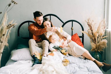 Üç kişilik mutlu bir aile yatakta oturuyor. Anne ve baba küçük oğullarına sarılıp birbirlerine gülümsüyorlar.