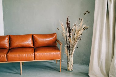 Süslü kahverengi kanepe geniş bir stüdyoda duruyor. Kuru dallı cam bir vazonun yanında.