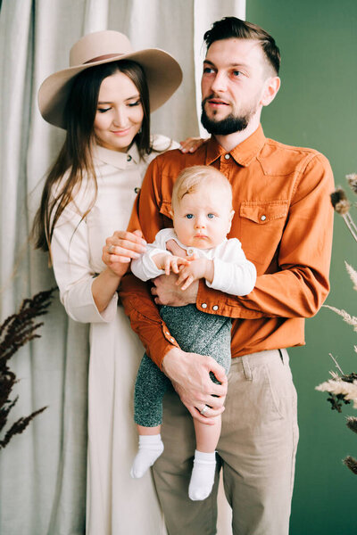 a beautiful young mother in a beige dress and hat, holding her stylishly dressed son in her arms