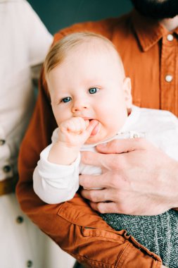Ailesinin kollarında küçük mutlu bir çocuk, bir fotoğraf çekiminde şık kıyafetler giymiş.