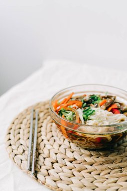 Bardakta Japon eriştesi çorbası, içinde vejetaryen malzemeler, küçük tabakta taze sebzeler, pirinç eriştesi, mantar ve miso ezmesi çorbası.