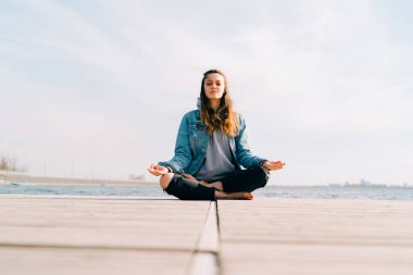 Genç ve güzel bir kız gölün yanındaki iskelede oturuyor ve meditasyon yapıyor.