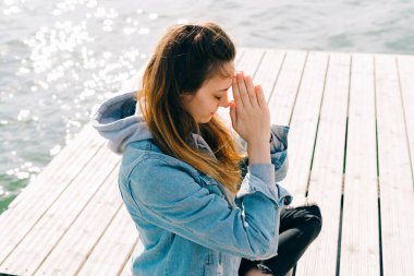 Genç ve güzel bir kız gölün yanındaki iskelede oturuyor ve meditasyon yapıyor.