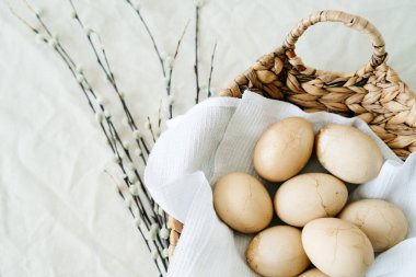 Doğal bir hasır sepetinde, beyaz bir peçetede çatallı birkaç Paskalya yumurtası vardır. Tomurcuklanan söğüt dallarıyla süslü, renkli bir tonda doğal kahveyle boyanmıştır. Paskalya konsepti.