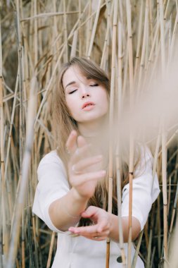 Açık beyaz elbiseli, siyah ayakkabılı çekici bir kızın portresi sazlıkların arasında duruyordu.